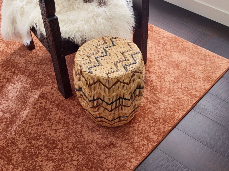 Wooden armchair in a room with dark hardwood flooring and a large orang patterned are rug - Carpet binding services from Carpet Innovations in Denver, CO